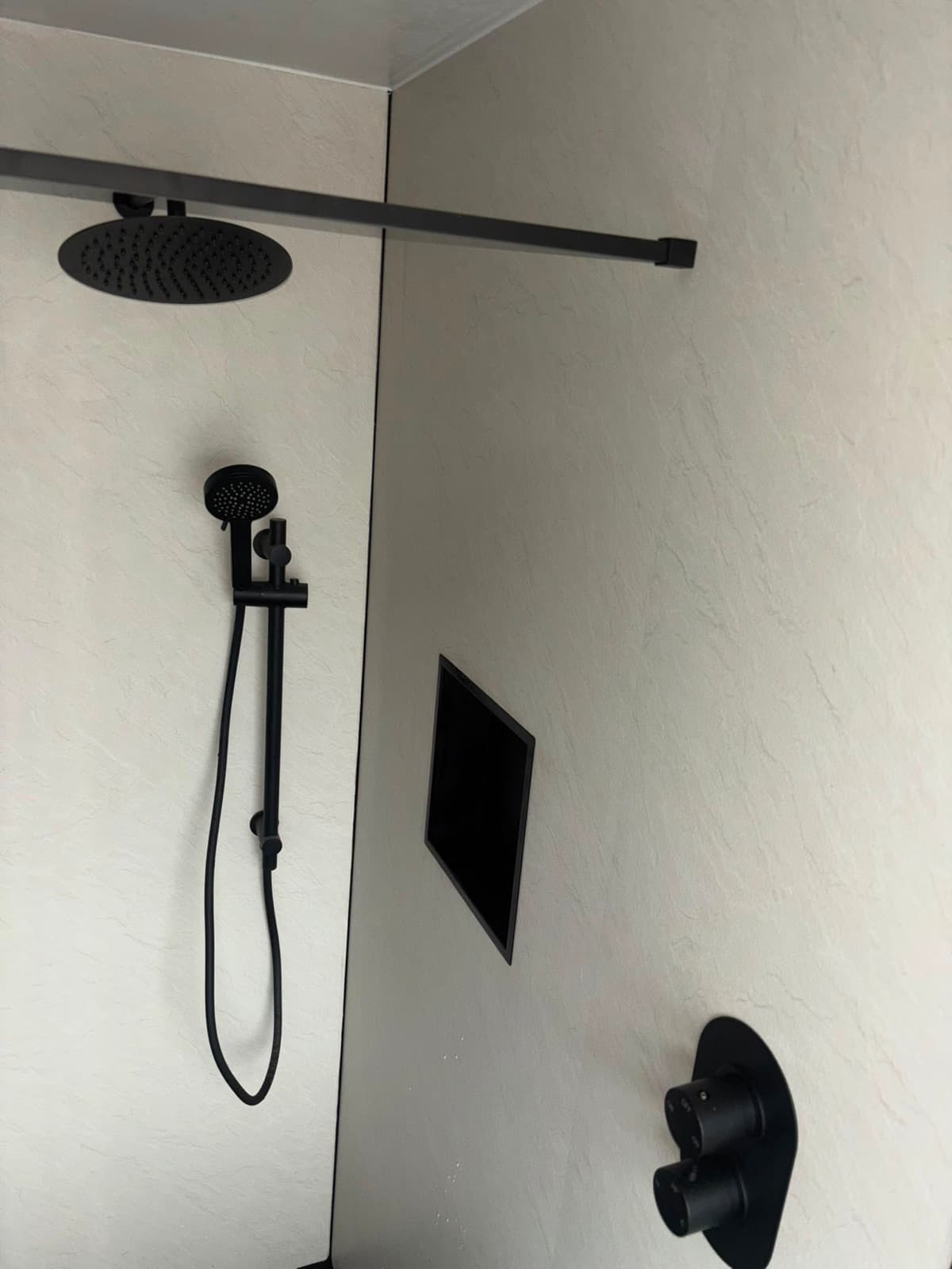 Black shower on a slim tiled wall