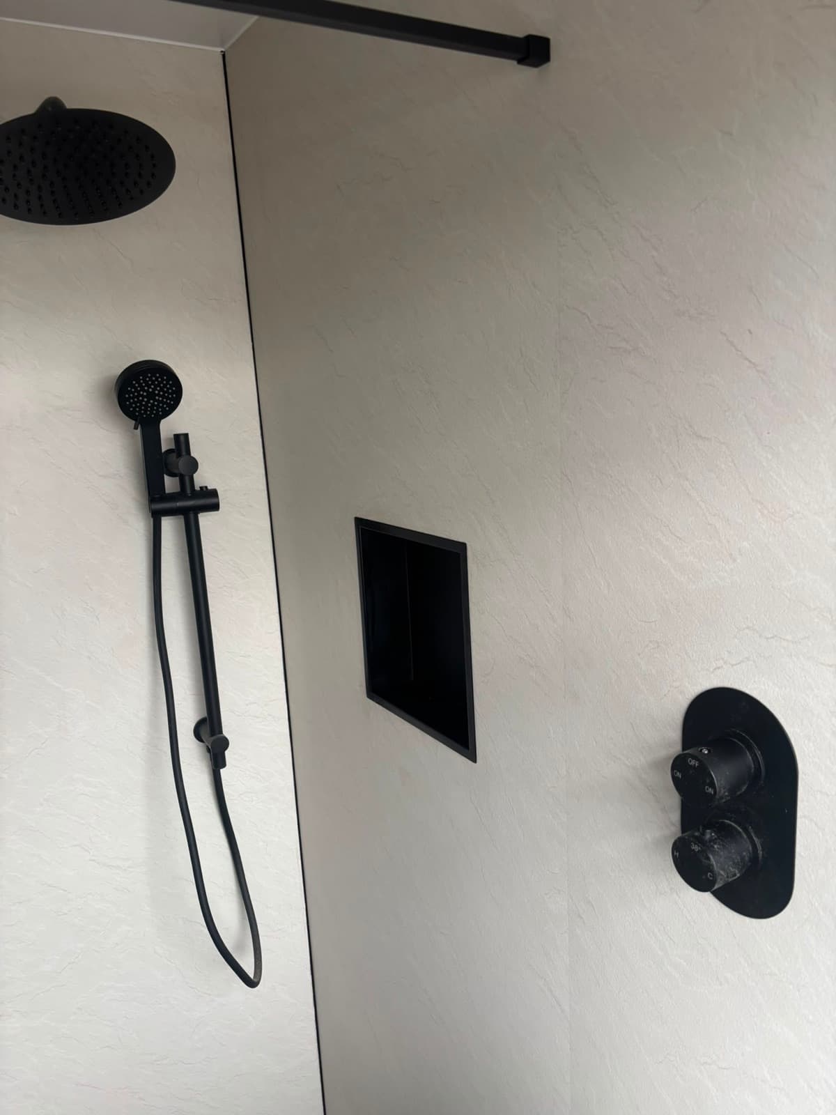 Black shower fittings on a wide tiled wall